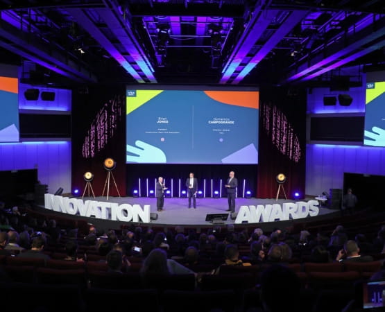 Trois personnes avec des microphones et un écran géant sur une scène avec des lettres géantes placées sur la scène devant une foule lors des INTERMAT Innovation Awards 2024
