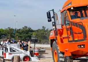 Group of people watching a demonstration of an orange construction machine 